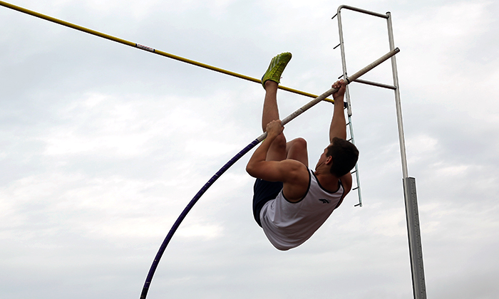 Pole vaulter preparing to clear the bar at a track meet.